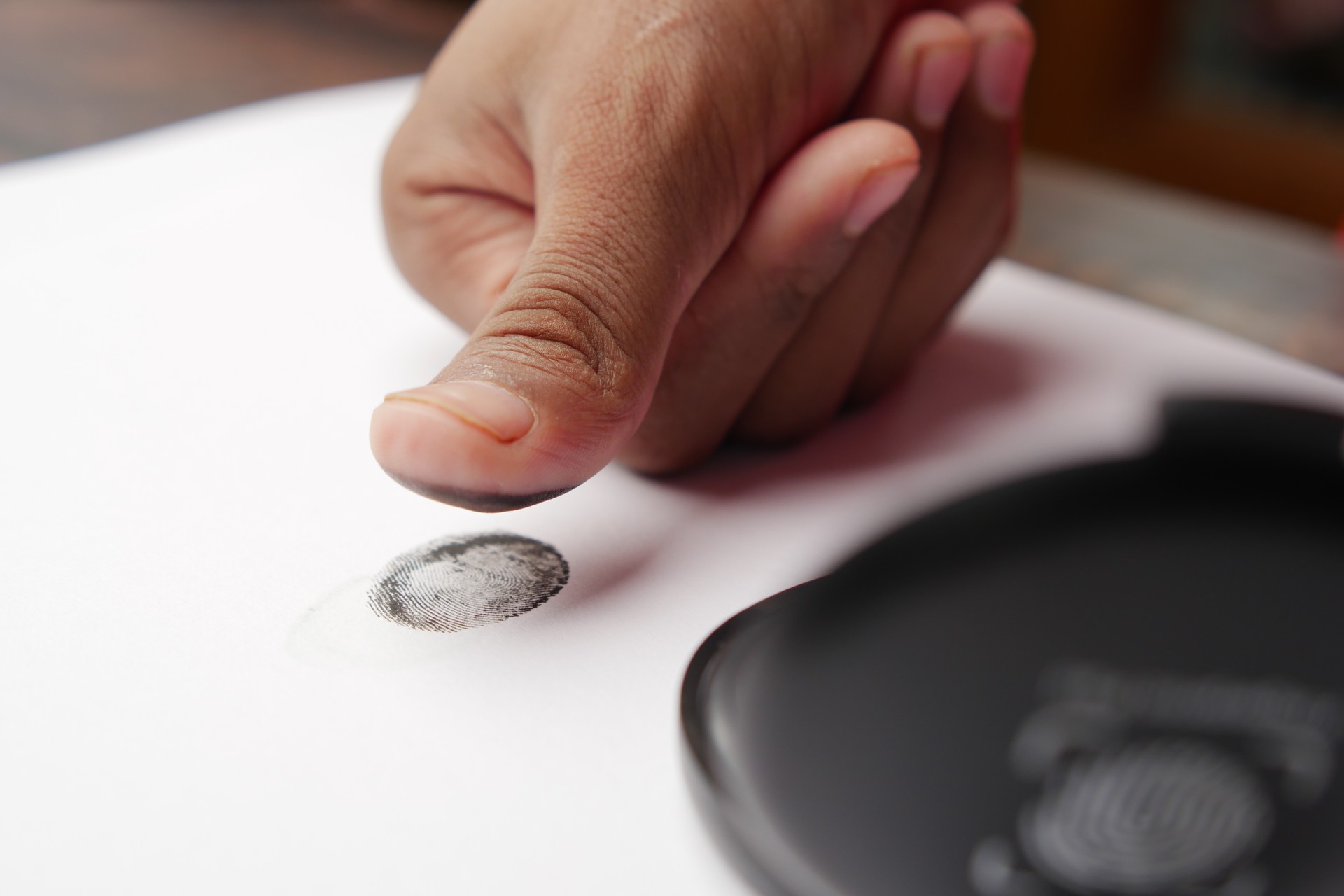 person hand putting black fingerprints on a paper close up ,